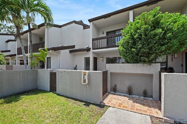 back of property with stucco siding, a balcony, and a gate