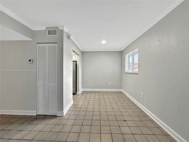 empty room with crown molding, a textured wall, baseboards, and light tile patterned floors
