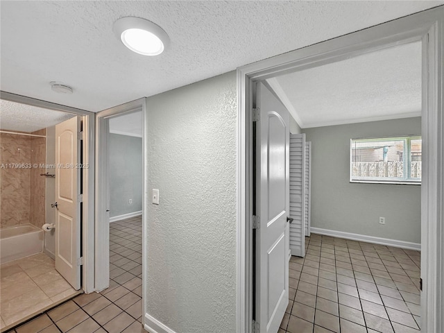 hall with a textured ceiling, light tile patterned floors, a textured wall, and baseboards