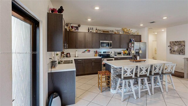 22986 SW 128th Pl, Miami, FL 33170 - kitchen with appliances with stainless steel finishes, light countertops, a kitchen breakfast bar, light tile patterned floors, and dark brown cabinetry