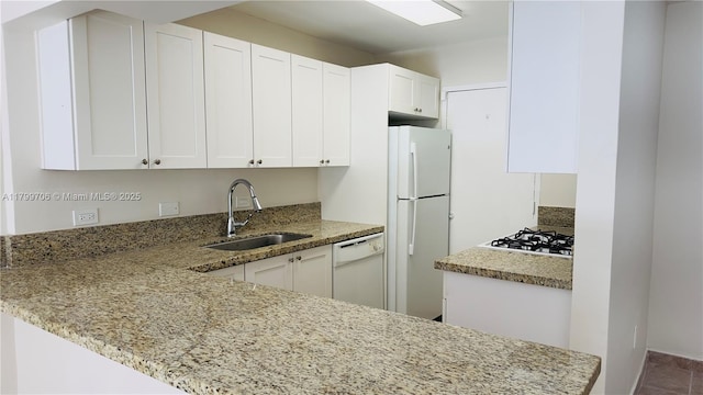 kitchen with white appliances, a sink, white cabinets, light stone counters, and a peninsula