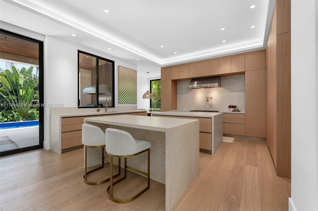 kitchen featuring modern cabinets, a center island, wall chimney exhaust hood, light wood-style flooring, and a sink