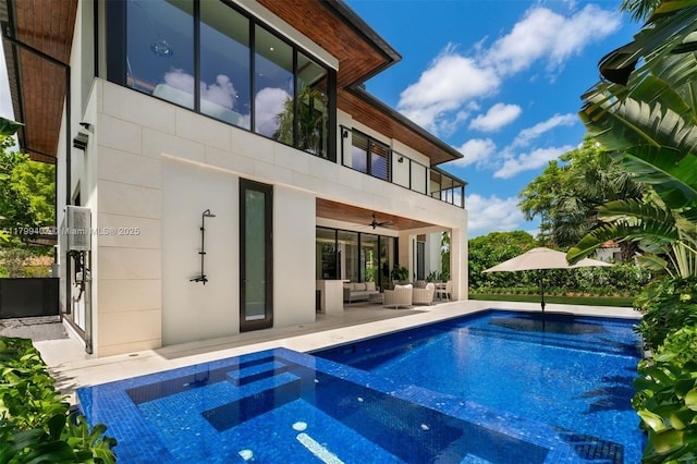 rear view of house with an outdoor living space, a ceiling fan, a pool with connected hot tub, a balcony, and a patio