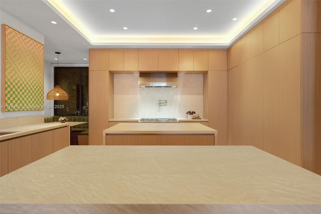 kitchen with wall chimney range hood, light brown cabinetry, modern cabinets, light countertops, and a kitchen island