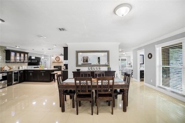 dining room with beverage cooler, crown molding, and light tile patterned flooring