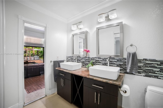 full bathroom with toilet, decorative backsplash, double vanity, crown molding, and ensuite bathroom