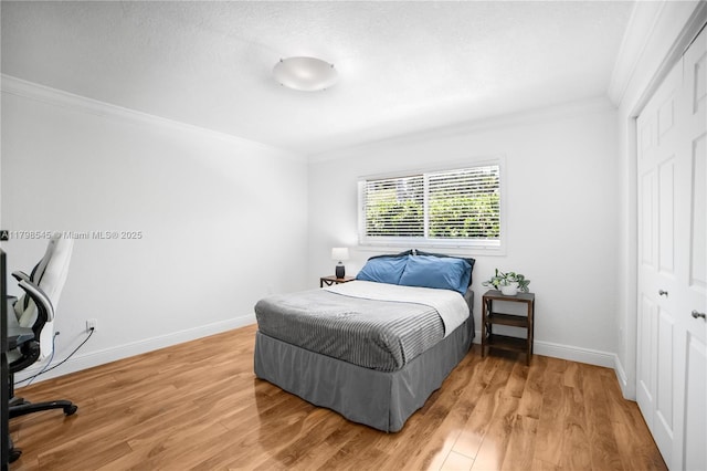 bedroom featuring ornamental molding, a closet, light wood finished floors, and baseboards