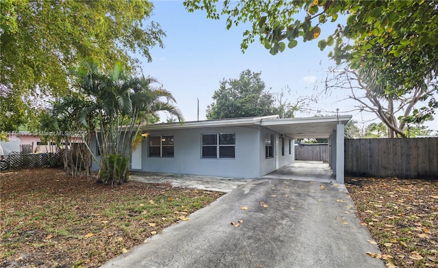 ranch-style house with asphalt driveway, fence, a carport, and stucco siding