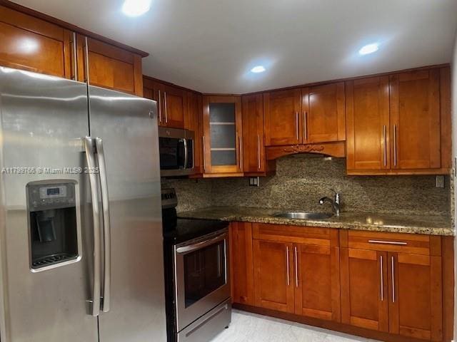 9920 NW 68th Pl Unit 103, Tamarac, FL 33321 - kitchen with appliances with stainless steel finishes, a sink, brown cabinetry, dark stone counters, and backsplash
