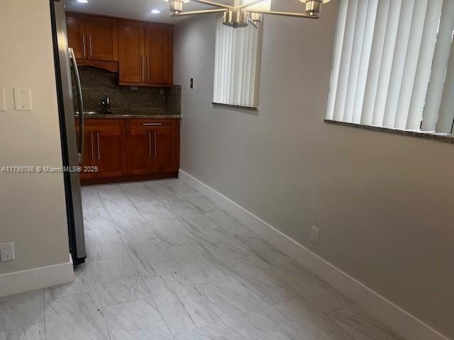 9920 NW 68th Pl Unit 103, Tamarac, FL 33321 - kitchen with brown cabinetry, a chandelier, baseboards, decorative backsplash, and light marble finish flooring
