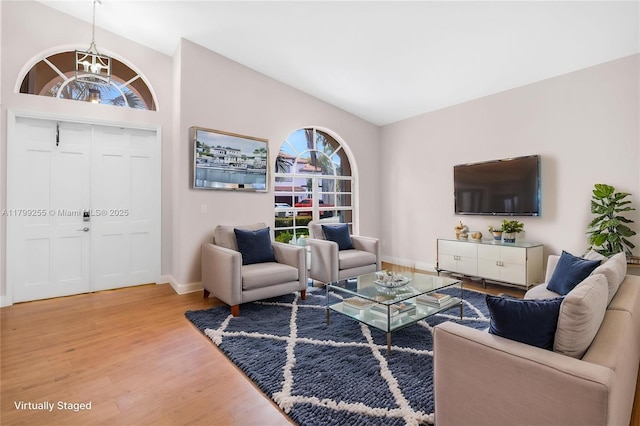 living room with light wood finished floors, vaulted ceiling, baseboards, and a chandelier