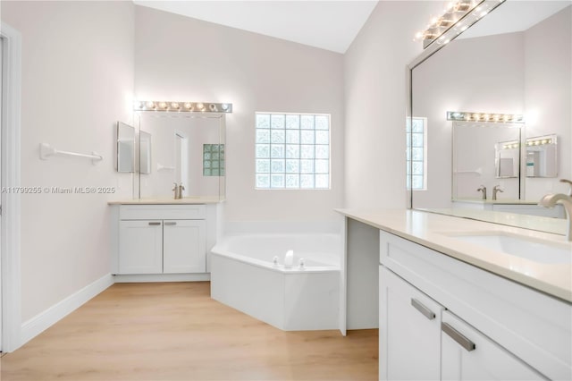 bathroom featuring wood finished floors, two vanities, and a bath