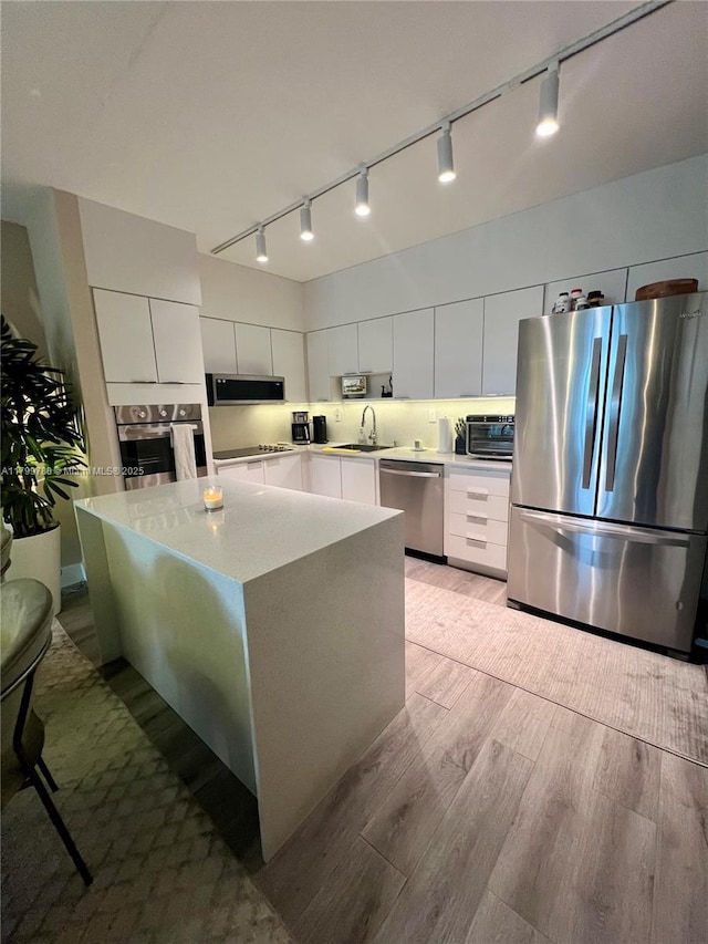 kitchen with appliances with stainless steel finishes, rail lighting, a sink, and light wood-style floors