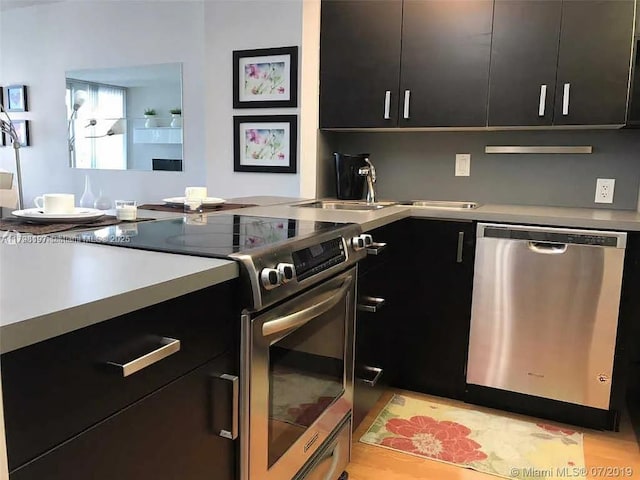kitchen with stainless steel appliances, dark cabinets, a sink, and light countertops