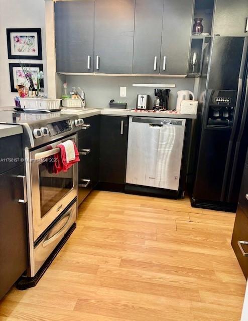 kitchen featuring stainless steel appliances, dark cabinets, light countertops, and light wood-type flooring