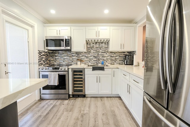 kitchen with stainless steel appliances, beverage cooler, light countertops, a sink, and white cabinetry
