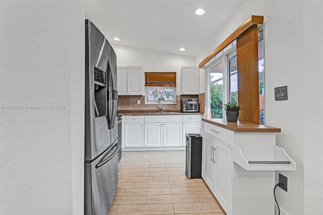 9821 W Fern Ln, Miramar, FL 33025 - kitchen featuring a textured wall, stainless steel appliances, white cabinets, backsplash, and vaulted ceiling
