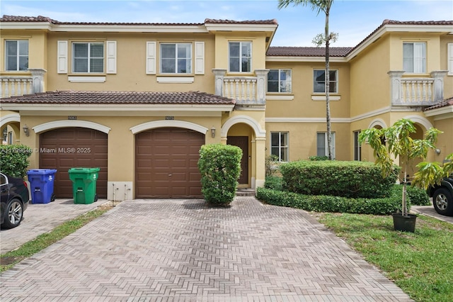 view of property with driveway, a balcony, a garage, and stucco siding