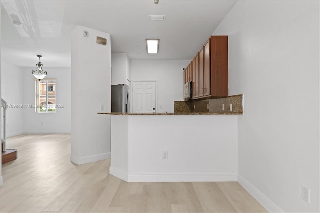 kitchen with stainless steel appliances, light wood-style flooring, and dark stone countertops