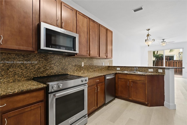kitchen featuring stainless steel appliances, a sink, a peninsula, decorative backsplash, and dark stone counters