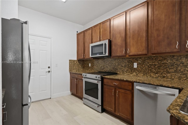 kitchen featuring appliances with stainless steel finishes, tasteful backsplash, light wood finished floors, dark stone counters, and baseboards