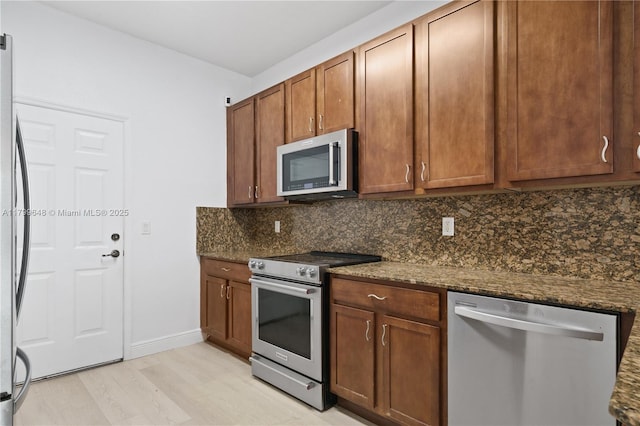 kitchen with appliances with stainless steel finishes, decorative backsplash, light wood finished floors, and dark stone counters