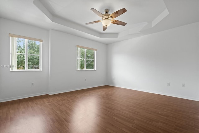 spare room featuring a tray ceiling, dark wood finished floors, a ceiling fan, and baseboards