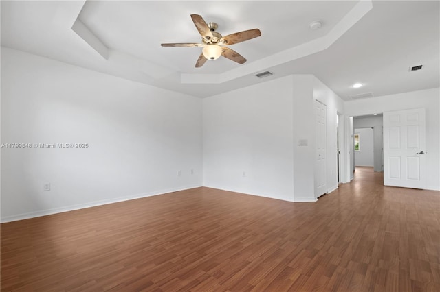 unfurnished room with a tray ceiling, a ceiling fan, wood finished floors, a smoke detector, and baseboards