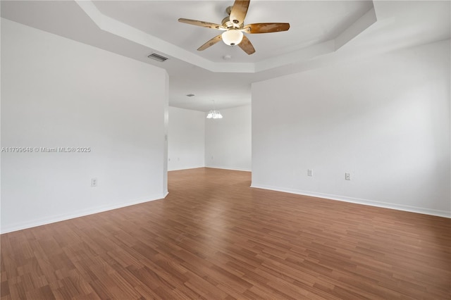 spare room with a raised ceiling, ceiling fan, wood finished floors, a chandelier, and baseboards