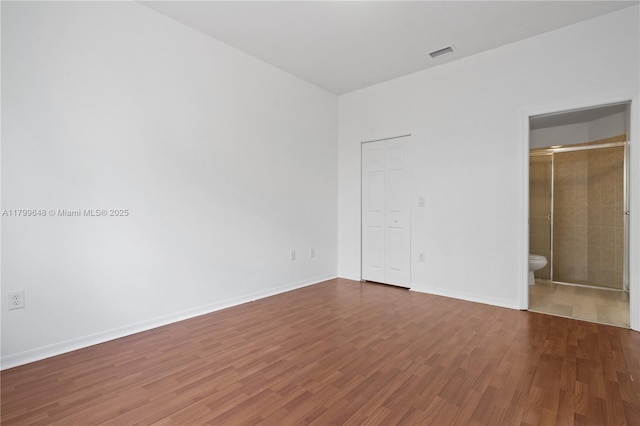 unfurnished bedroom featuring wood finished floors, baseboards, and connected bathroom