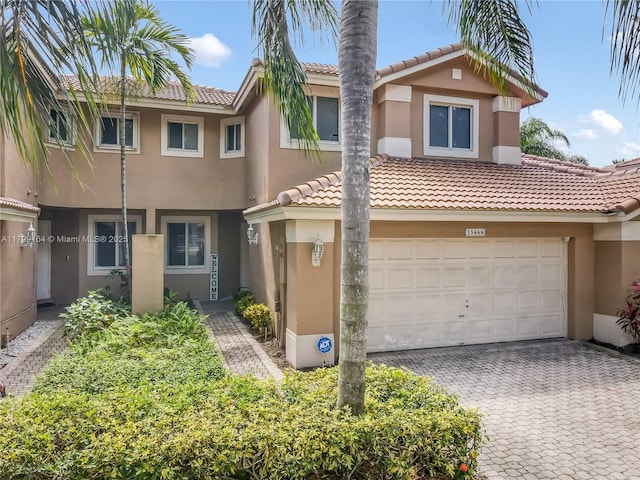townhome / multi-family property with a tiled roof, stucco siding, a garage, and decorative driveway