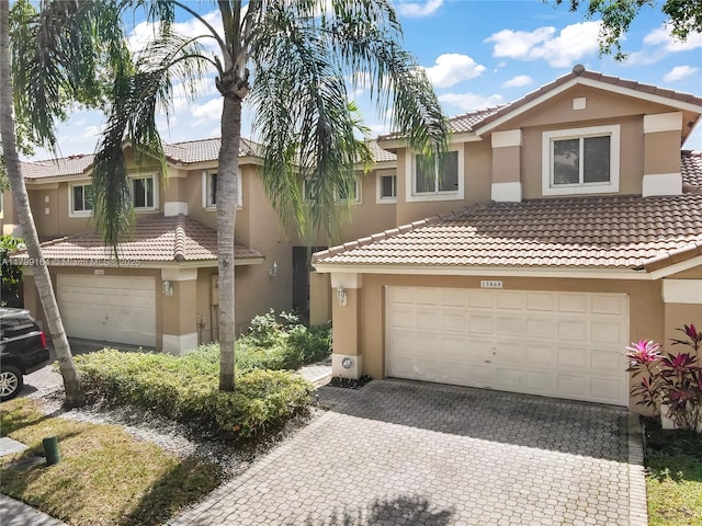 multi unit property with stucco siding, decorative driveway, a tiled roof, and a garage