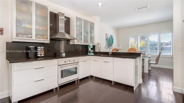 kitchen with white oven, wall chimney exhaust hood, a sink, a peninsula, and baseboards