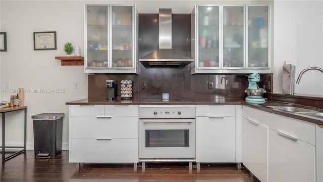 kitchen with oven, wall chimney range hood, modern cabinets, a sink, and tasteful backsplash