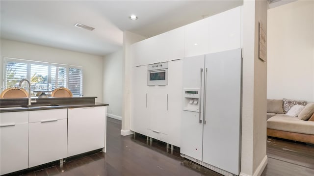 kitchen featuring white appliances, a sink, dark wood-style floors, dark countertops, and recessed lighting
