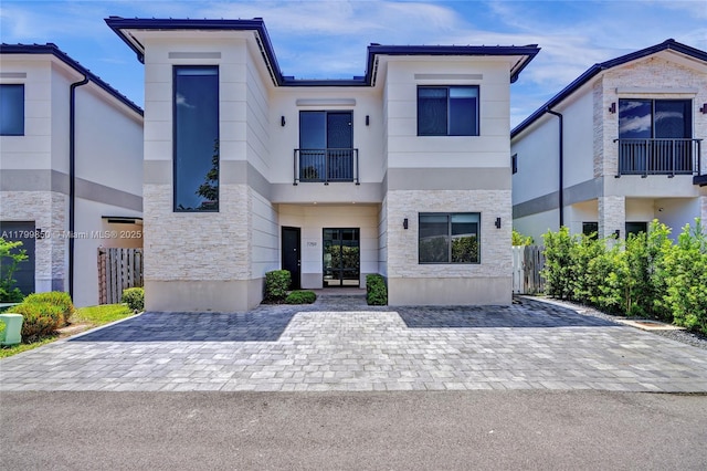 contemporary home featuring a balcony, stone siding, fence, and stucco siding