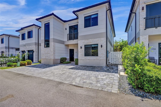 contemporary house with a balcony, stone siding, a gate, and fence