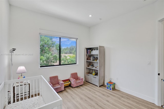 bedroom featuring wood finished floors, a nursery area, baseboards, and recessed lighting