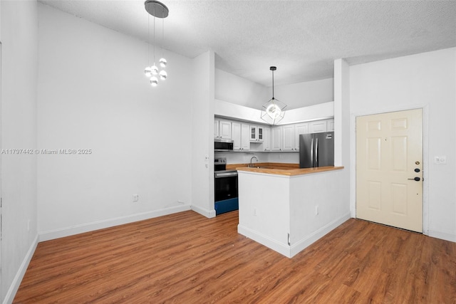933 NE 199th St Unit 207, Miami, FL 33179 - kitchen featuring appliances with stainless steel finishes, a peninsula, wood finished floors, a textured ceiling, and baseboards