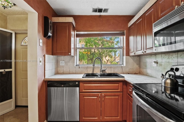 450 SE 7th St Unit 230, Dania Beach, FL 33004 - kitchen featuring stainless steel appliances, a sink, tasteful backsplash, tile patterned flooring, and brown cabinets