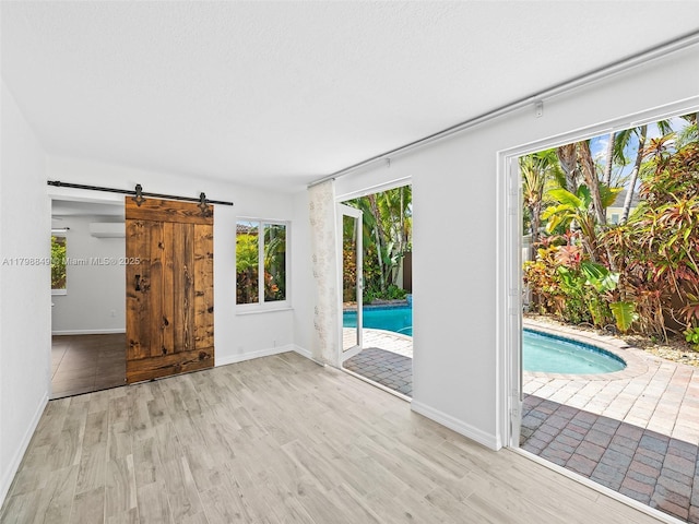 1730 NE 16th St, Fort Lauderdale, FL 33304 - empty room featuring wood finished floors, a wall mounted air conditioner, a barn door, and baseboards