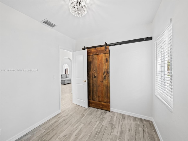 1730 NE 16th St, Fort Lauderdale, FL 33304 - unfurnished bedroom featuring light wood finished floors, baseboards, arched walkways, and a barn door
