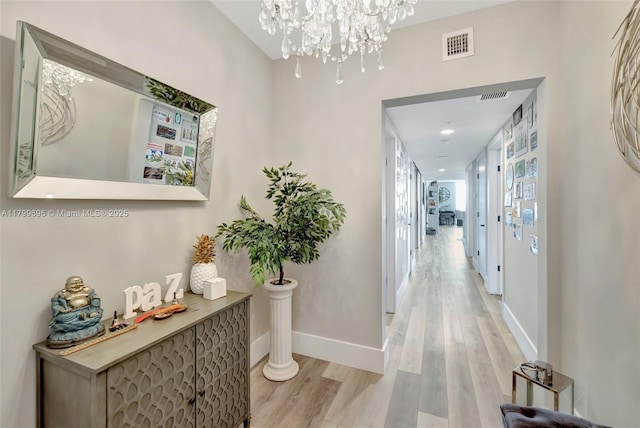 corridor featuring light wood finished floors, baseboards, and a chandelier