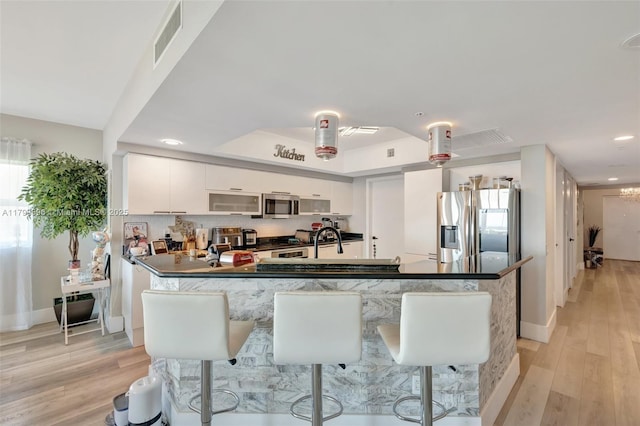 kitchen with appliances with stainless steel finishes, white cabinetry, light wood-style flooring, dark countertops, and recessed lighting