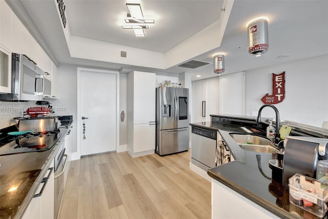 kitchen featuring stainless steel appliances, dark countertops, a sink, and light wood finished floors