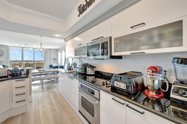 kitchen with appliances with stainless steel finishes, dark countertops, white cabinetry, and backsplash
