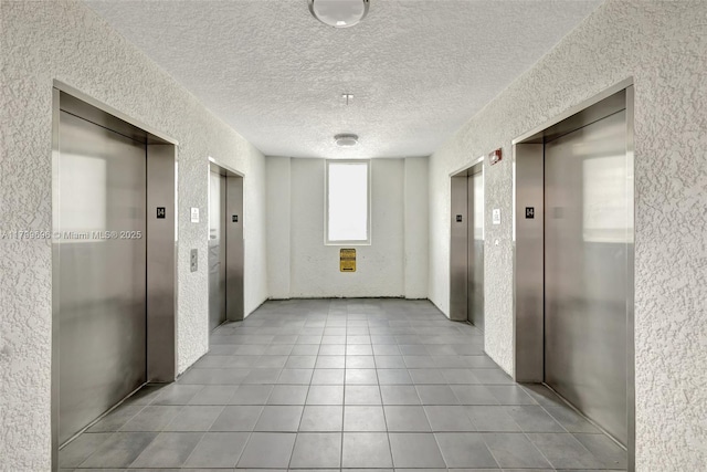 hall with elevator, a textured wall, tile patterned floors, and a textured ceiling