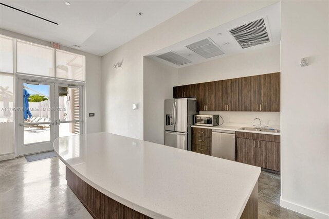 kitchen featuring stainless steel appliances, light countertops, a sink, concrete floors, and a kitchen island