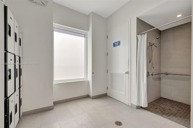 bathroom with tiled shower, baseboards, and tile patterned flooring