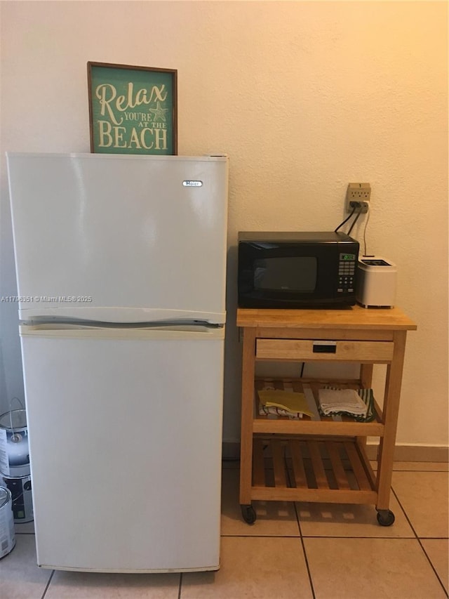 kitchen featuring freestanding refrigerator, black microwave, tile patterned floors, and baseboards